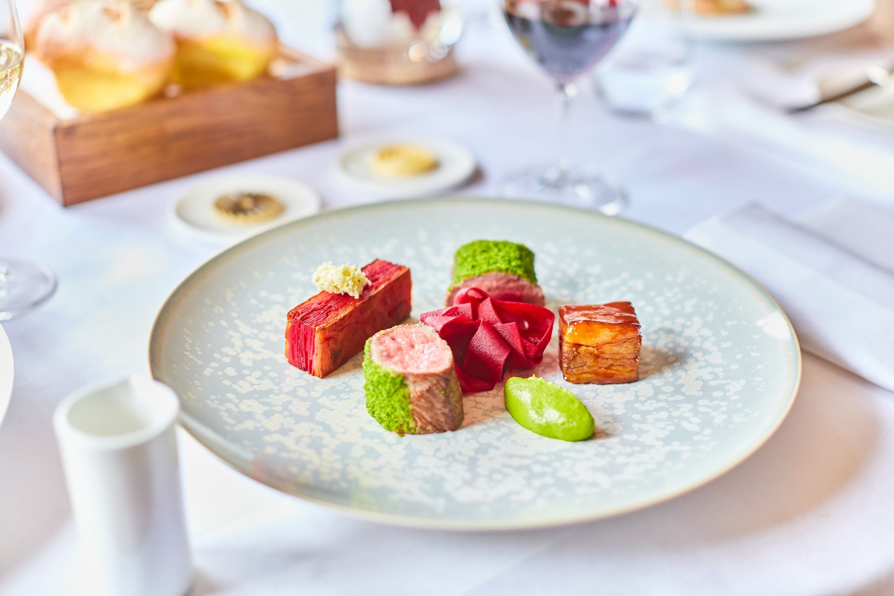 Une assiette contenant divers aliments, notamment une tranche de viande et un légume vert, est posée sur une table recouverte d’une nappe blanche.