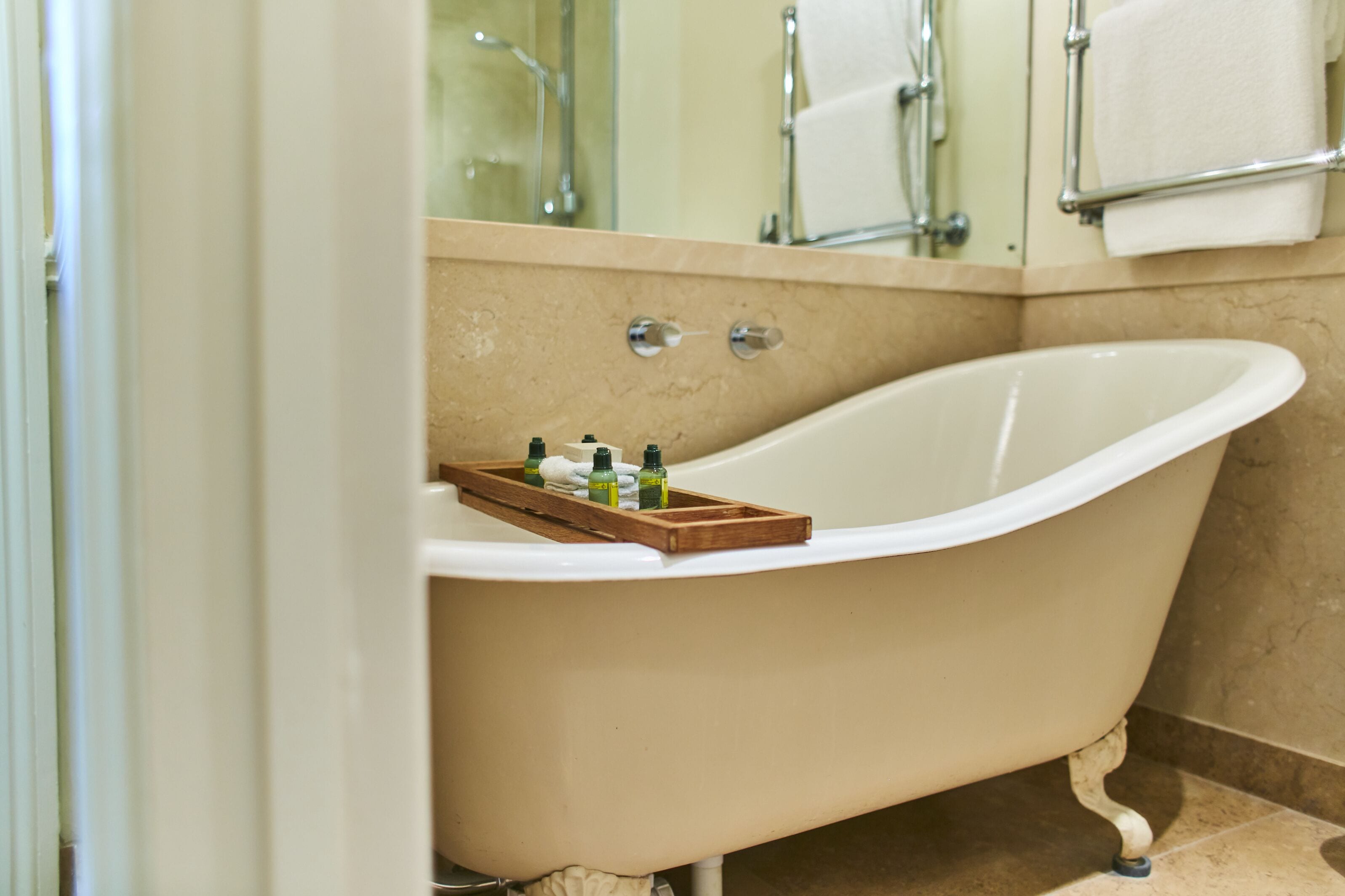 Een badkamer met een vrijstaand bad, een houten dienblad met toiletartikelen en een handdoekhouder.
