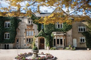 A historic building with ivy-covered walls, a central entrance with a wooden door, and a gravel courtyard with a fountain. - The Bath Priory Hotel and Spa (Bath)