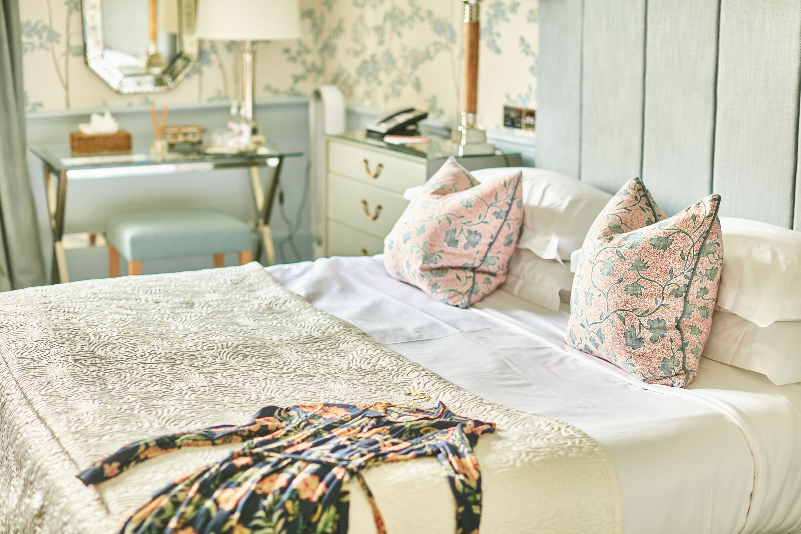 Una cama bien hecha con almohadillas estampadas, una colcha decorativa y una mesita de noche con lámpara.