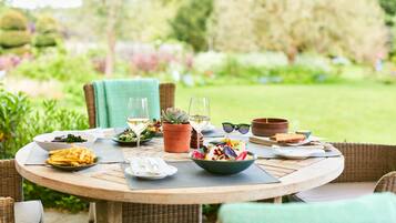 A round wooden table set outdoors with various dishes, glasses, and a potted plant.
