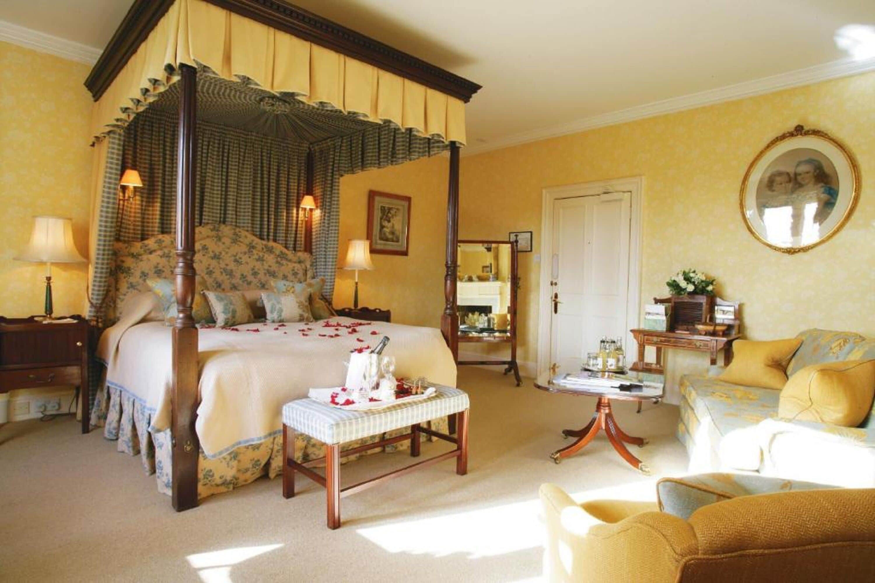 A four-poster bed with a canopy, a bedside table, a chair, and a small table with a lamp.