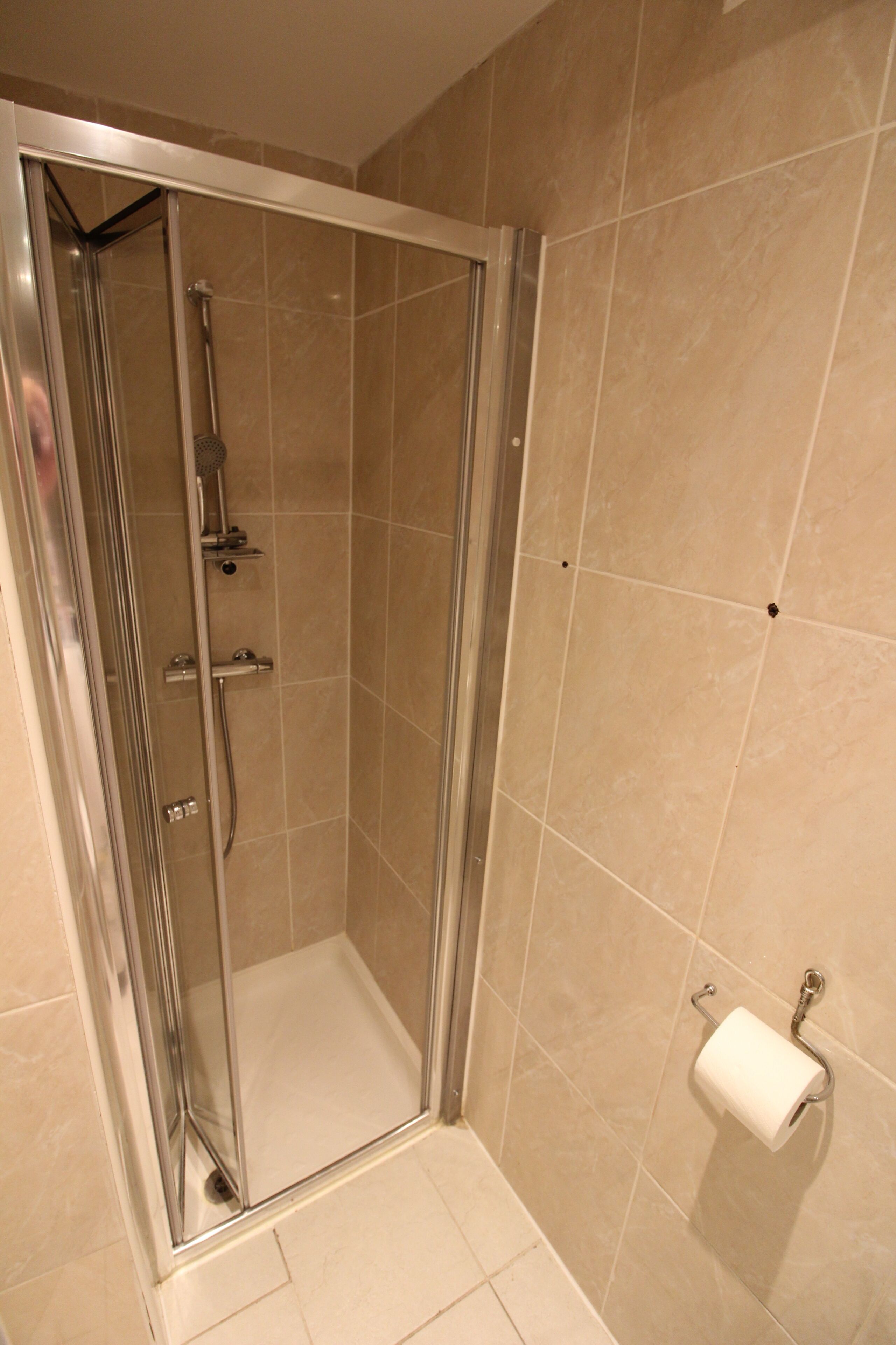A glass-enclosed shower stall with a handheld showerhead and a wall-mounted faucet.