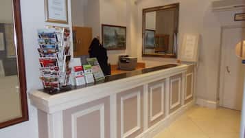 Een receptiebalie met een lijst in een lijst, een spiegel en een prikbord met reisbrochures.