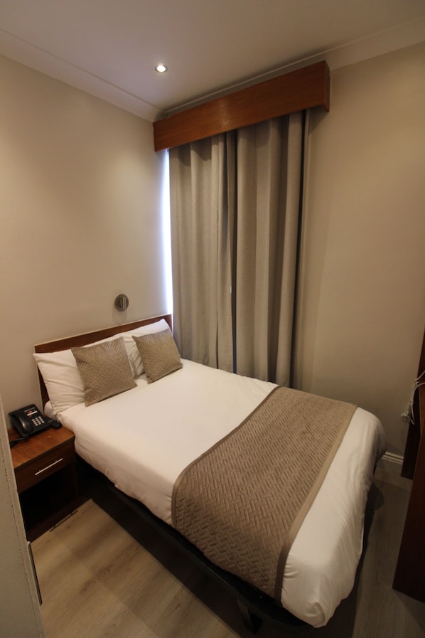 A hotel room with a bed, a nightstand, a telephone, and a window with curtains. - Wedgewood Hotel (London)