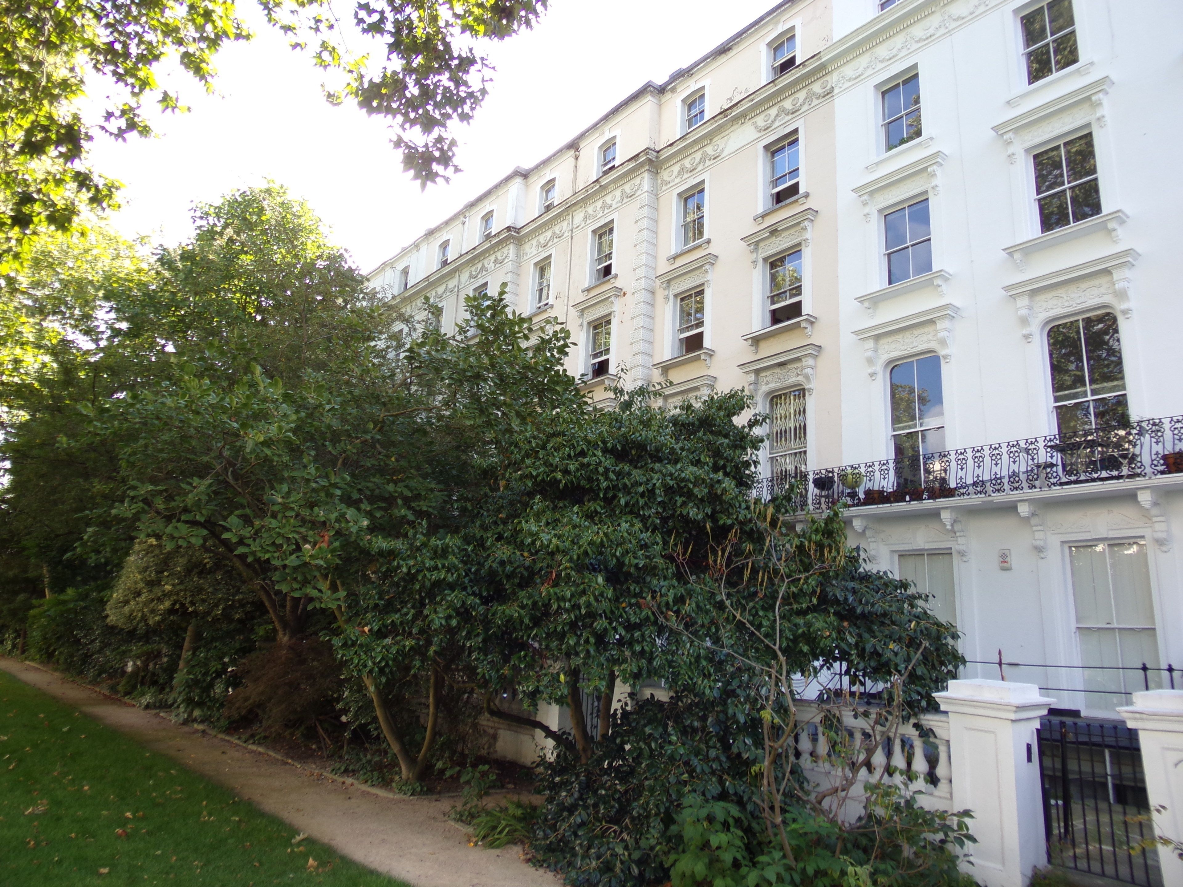 A row of white buildings with ornate window frames and a balcony with wrought iron railings.