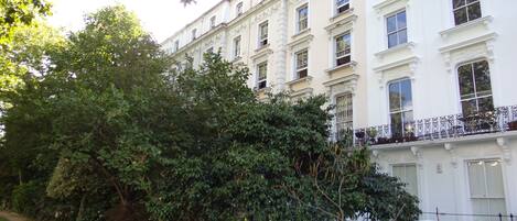 A row of white buildings with ornate window frames and a balcony with wrought iron railings.