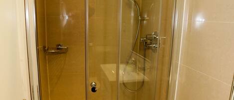 Une cabine de douche fermée par des parois en verre, avec une serviette blanche accrochée à la poignée de la porte.