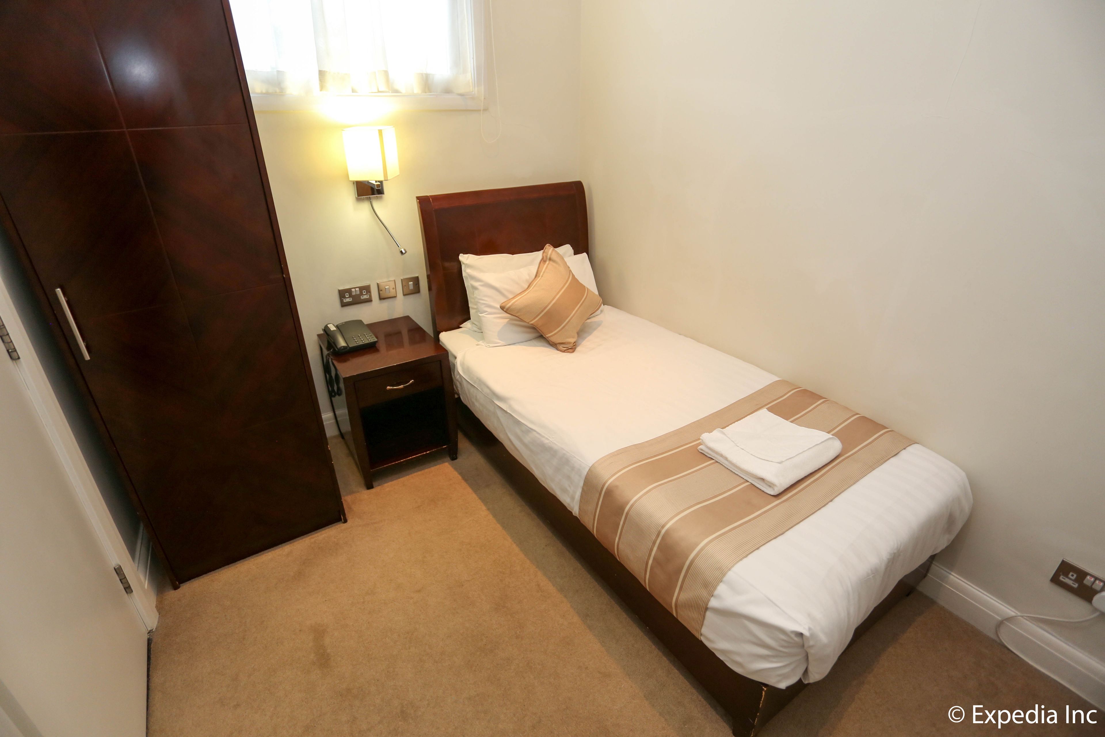 A hotel room with a single bed, a bedside table, a nightstand, a lamp, and a wardrobe.