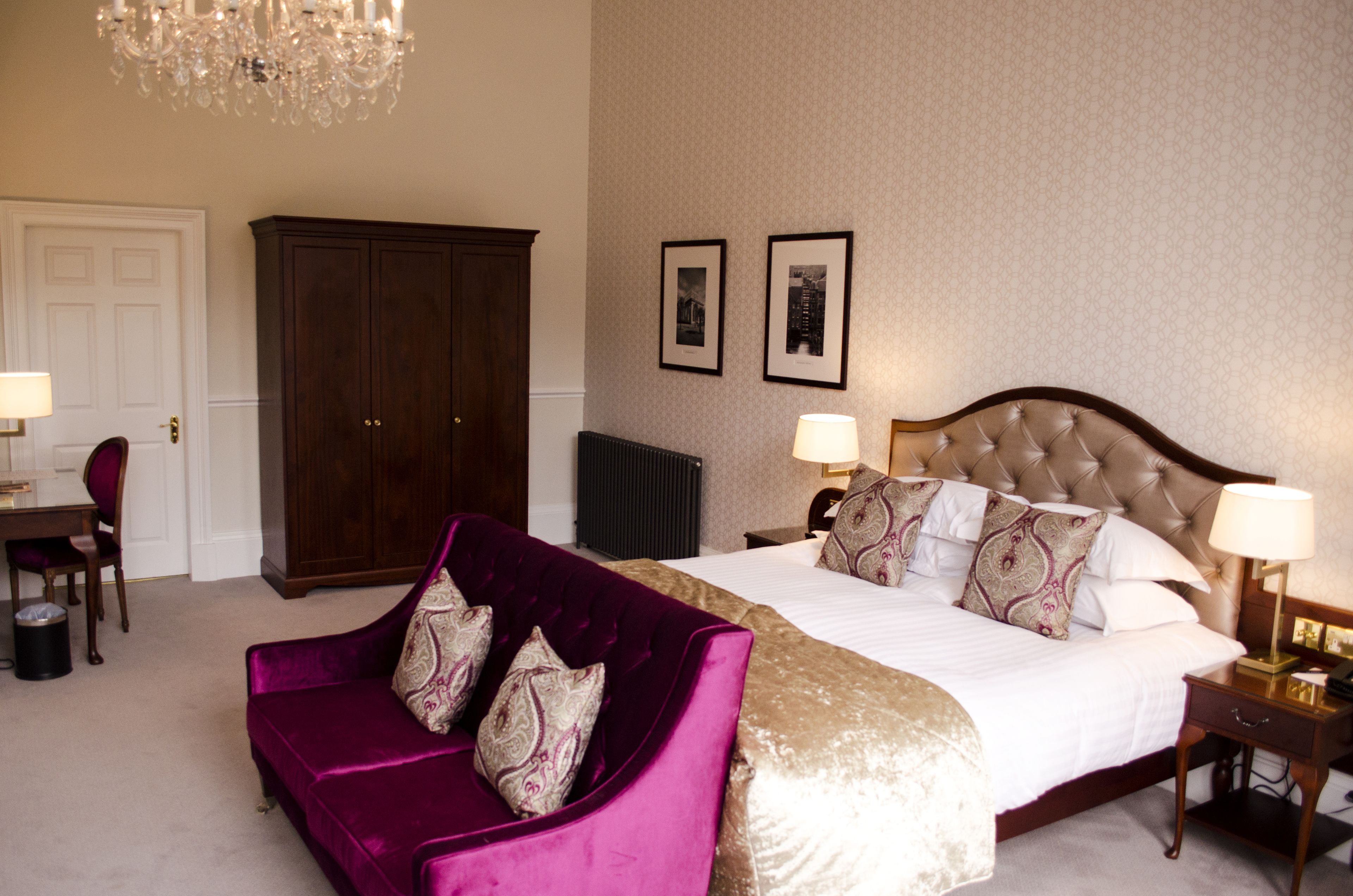 Ein Hotelzimmer mit einem großen Bett, einem violetten Samarsofa, einem Holzschrank und zwei gerahmten Bildern an der Wand.