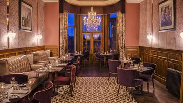 A formal dining area with leather seating, tables set with fine china, and a large chandelier.