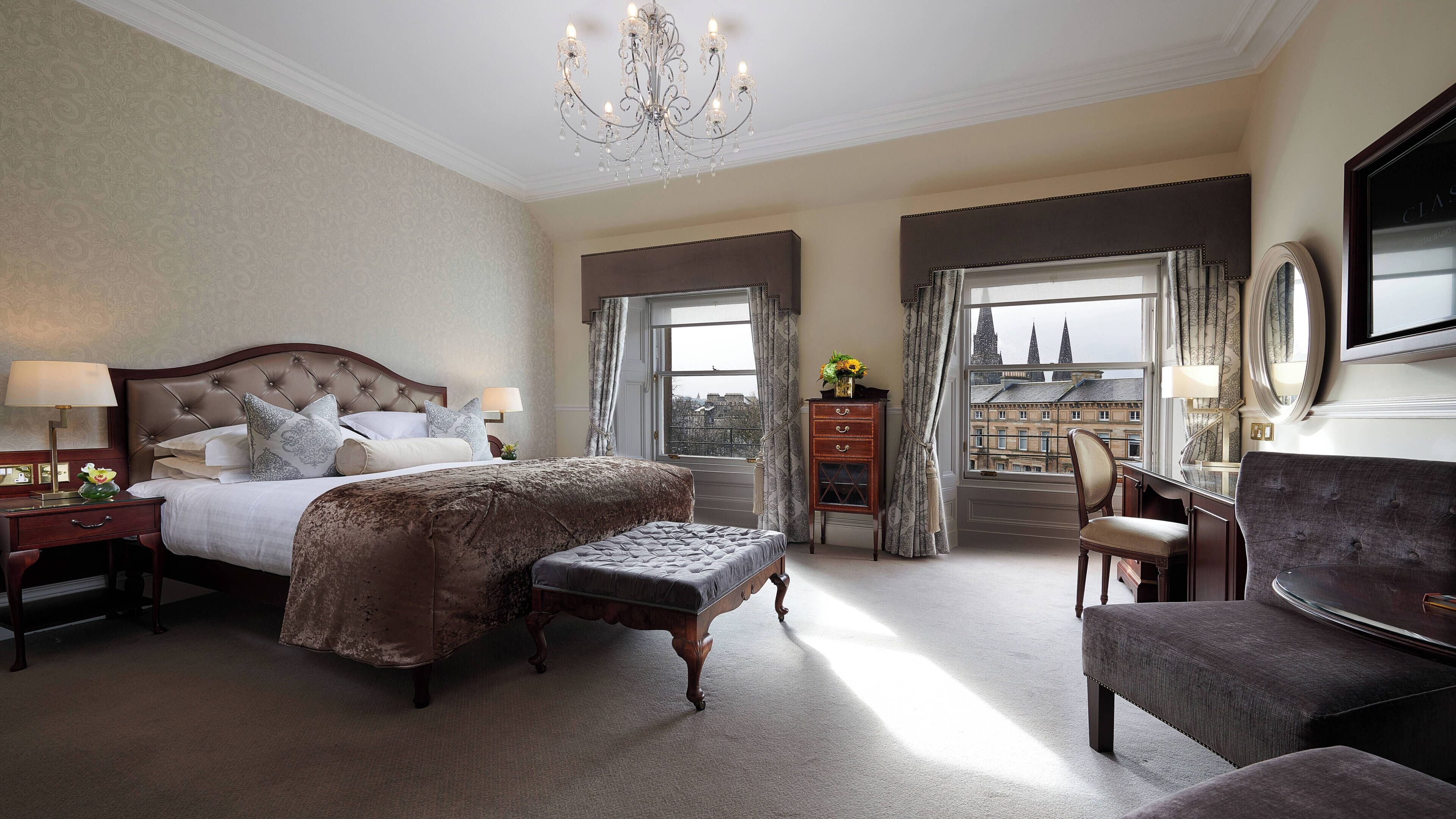 Een ruime slaapkamer met een groot bed, een zithoek met een stoel, en uitzicht op de stad vanuit het raam.