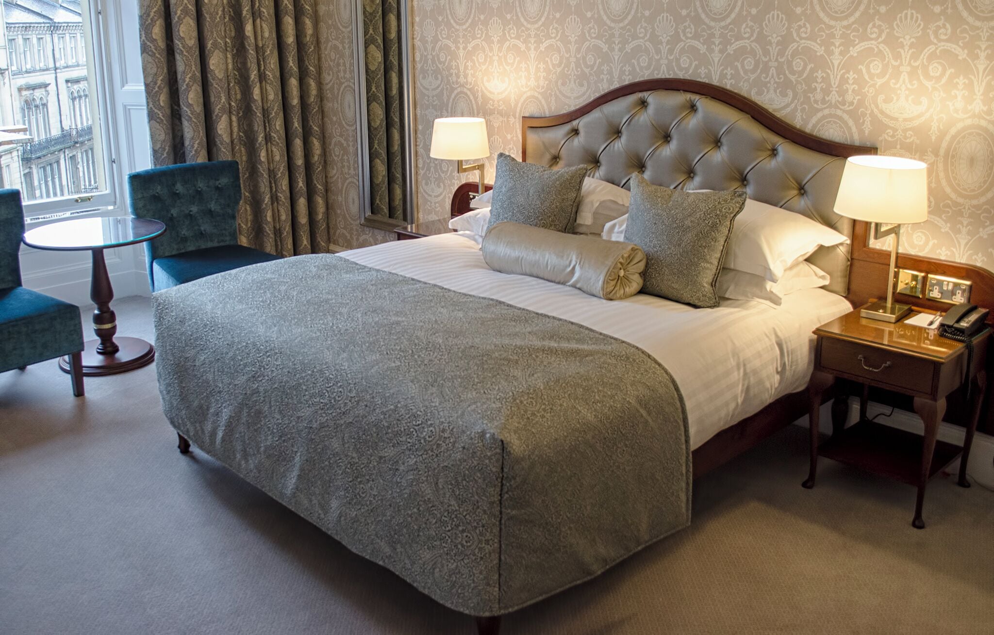 Een hotelkamer met een groot bed, twee nachtkastjes, een stoel en uitzicht op de stad.