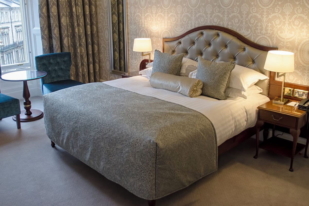 Een hotelkamer met een groot bed, twee nachtkastjes, een stoel en uitzicht op de stad.
