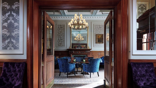 Een elegante eetzaal met een kroonluchter, blauwe gestoffeerde stoelen en een houten tafel.