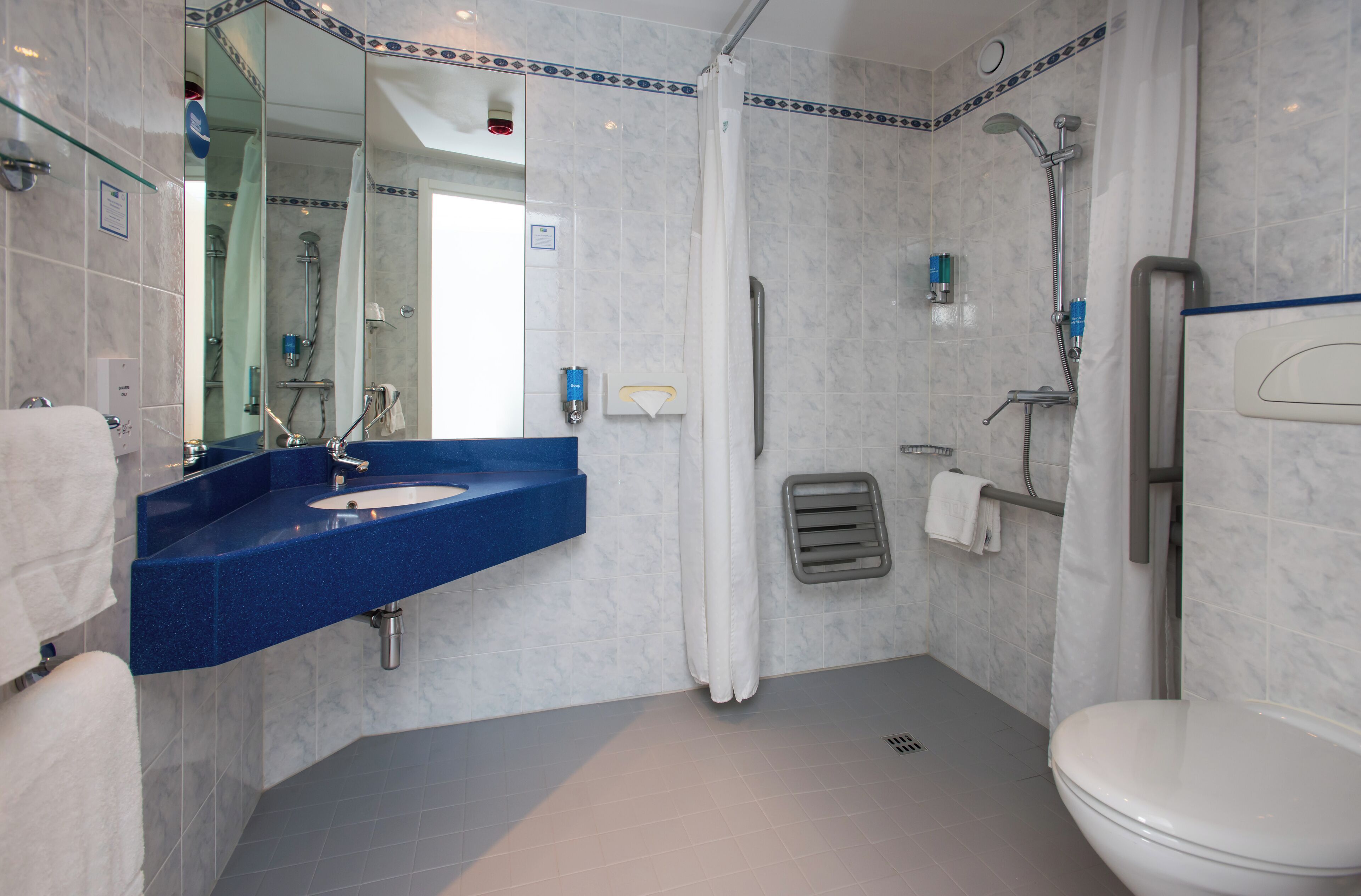 A modern bathroom with a blue sink, a toilet, and a shower area.