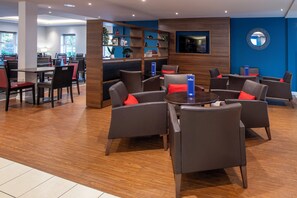 A modern hotel lobby with a wooden floor, comfortable seating areas, and a blue accent wall. - Holiday Inn Express Birmingham - Oldbury by IHG (Oldbury)
