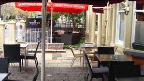 An outdoor seating area with tables and chairs, a sign for Whites Hotel, and a red umbrella. - Whites Hotel (Newcastle-upon-Tyne)