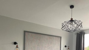 A modern bedroom with a large bed, a nightstand, a geometric wall art piece, and two pendant lights. - Whites Hotel (Newcastle-upon-Tyne)