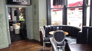 A BLANC lounge with a black leather sofa, two chairs, and a wooden table. - Whites Hotel (Newcastle-upon-Tyne)