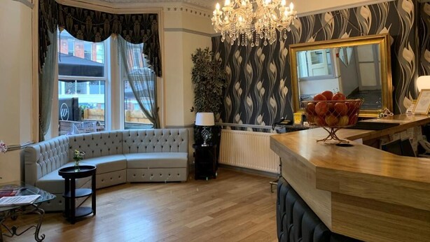 A living room with a curved sofa, a chandelier, a large mirror, and a fruit basket on a wooden counter. - Whites Hotel (Newcastle-upon-Tyne)