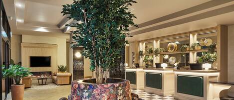 A lobby with a large tree, seating area, and a reception desk with plants.