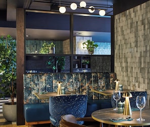 A modern restaurant interior with a blue booth seating, a round table with a gold finish, and a decorative wall with a brick pattern.