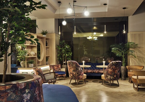 A modern lounge area with seating, plants, and a large mirror.