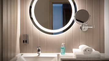 Een moderne badkamer met een witte wastafel, een ronde spiegel met verlichting, en een handdoek op het aanrecht.
