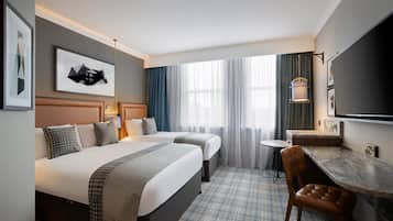 A hotel room with two beds, a desk, a chair, a TV, and a window with curtains.