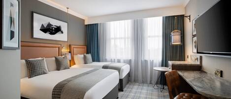 A hotel room with two beds, a desk, a chair, a TV, and a window with curtains.