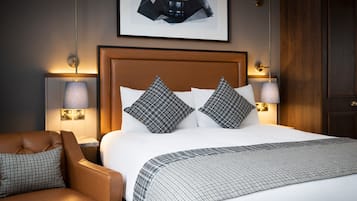 A hotel room with a large bed, two bedside lamps, a brown leather armchair, and a framed picture on the wall.