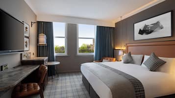 A hotel room with a bed, a desk, a chair, a TV, and a window with curtains.
