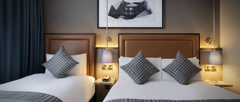 Habitación de hotel con dos camas, cada una con cabecero, mesitas de noche y lámparas. Encima de las camas hay un cuadro enmarcado en la pared.