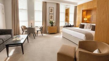 A hotel room with a bed, a sofa, a dining table with chairs, a coffee table, and a side table with a lamp.