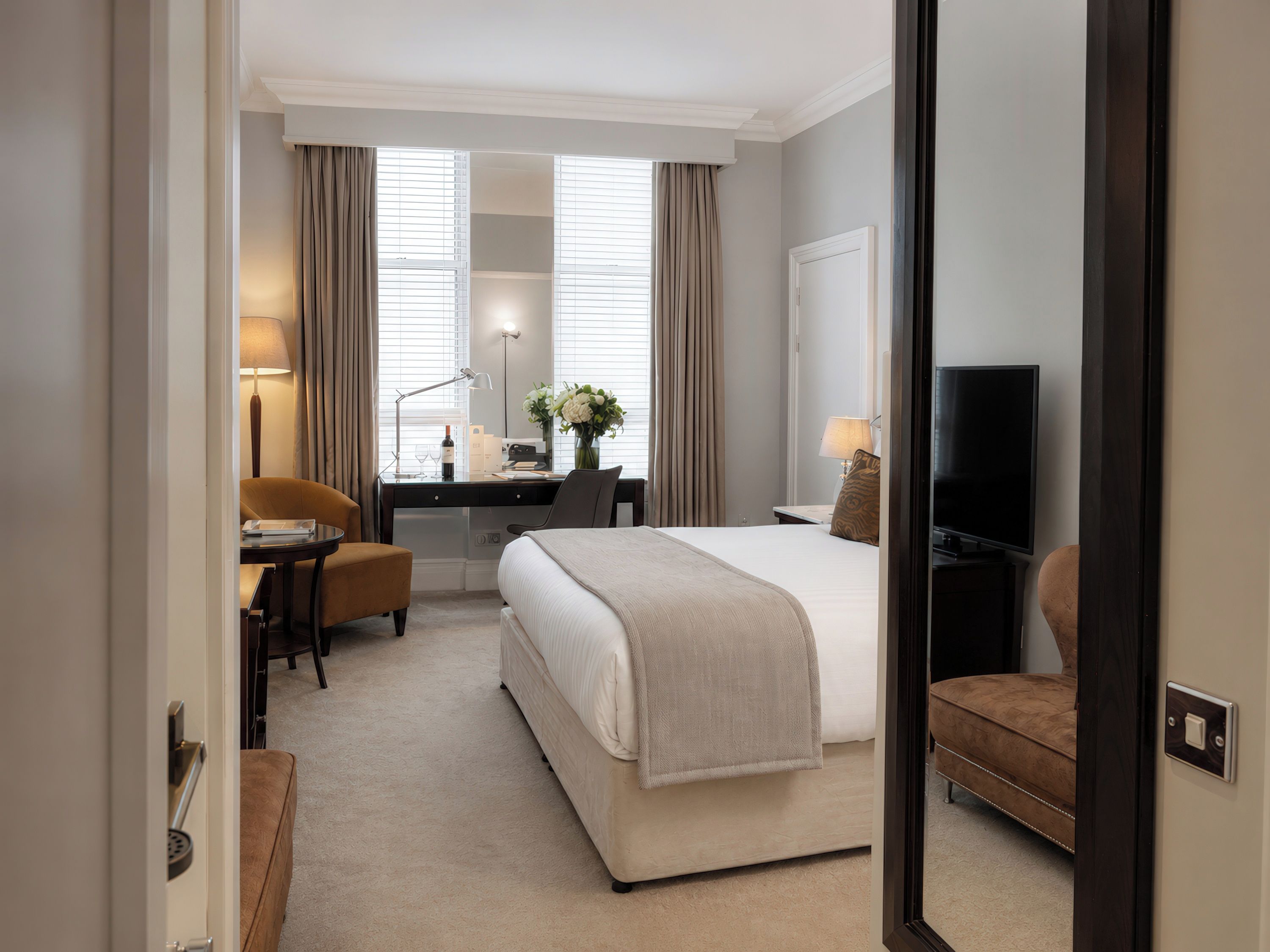 A hotel room with a bed, a desk, a chair, a television, and a mirror.