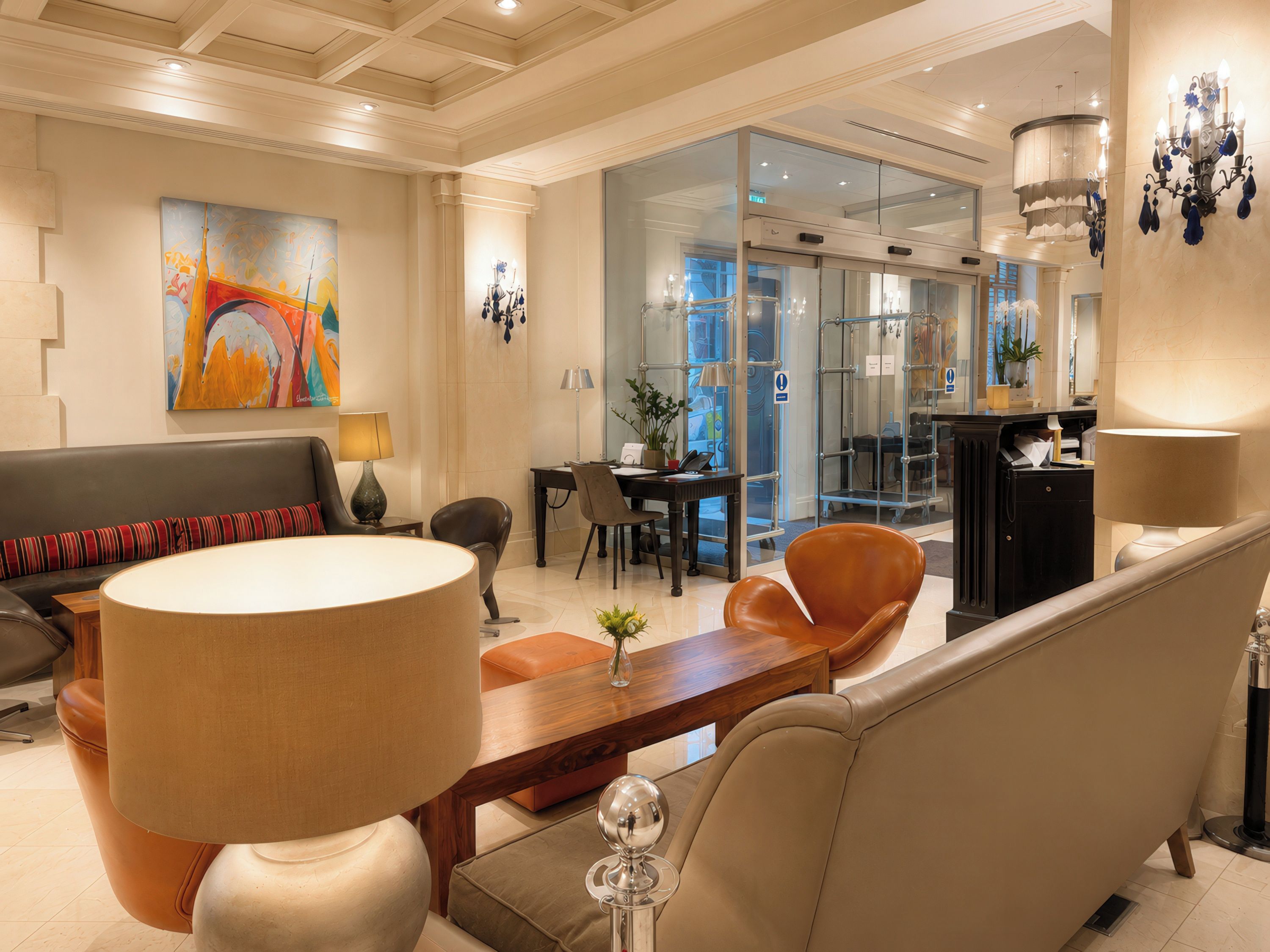 Un hall d’hôtel avec un canapé, des fauteuils, une table et une cloison en verre.