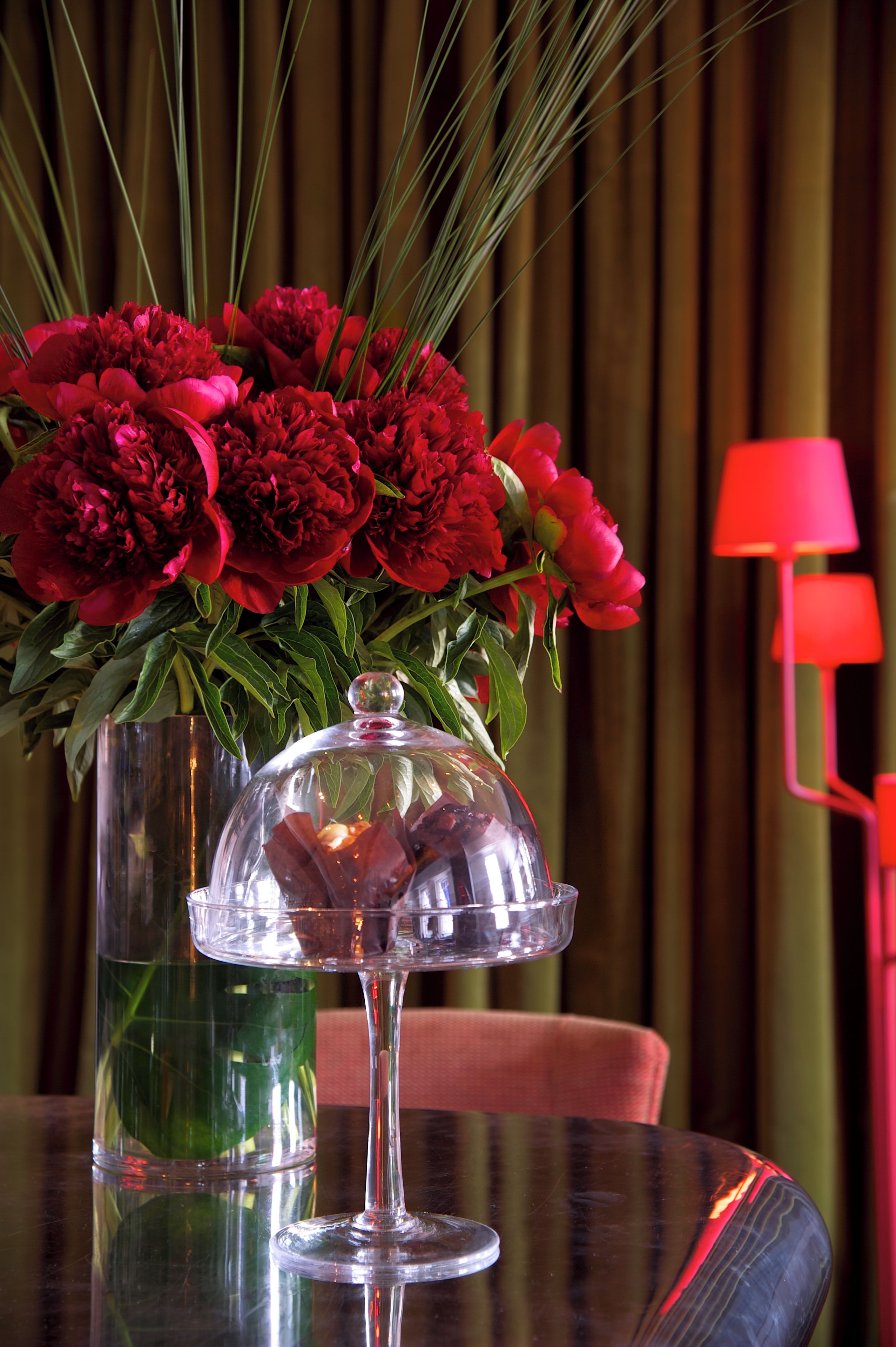 Une table sur laquelle se trouve un vase en verre contenant des fleurs rouges, le tout recouvert d’un cloche de verre.