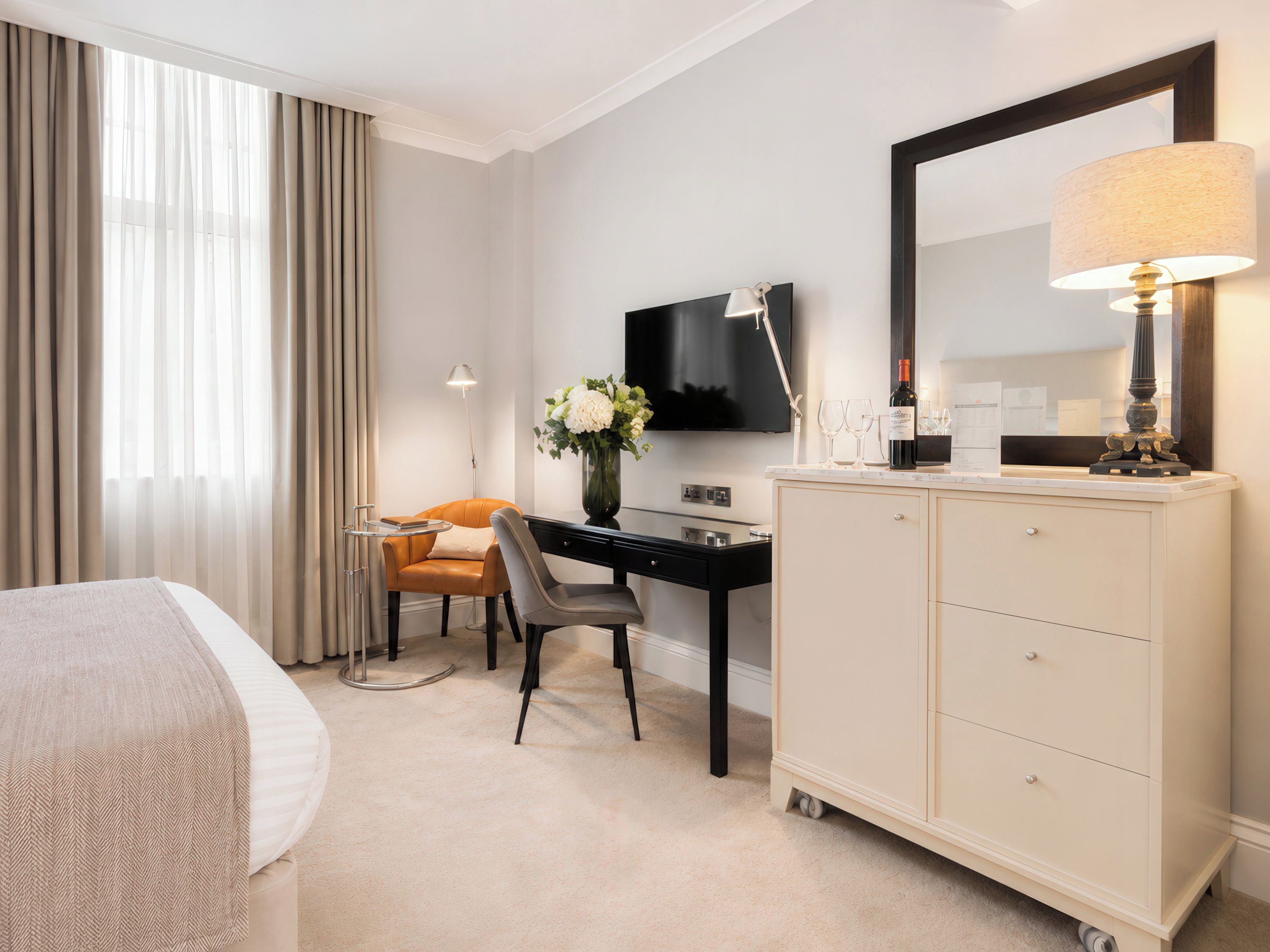 A hotel room with a bed, a desk, a chair, a television, a mirror, and a cabinet.