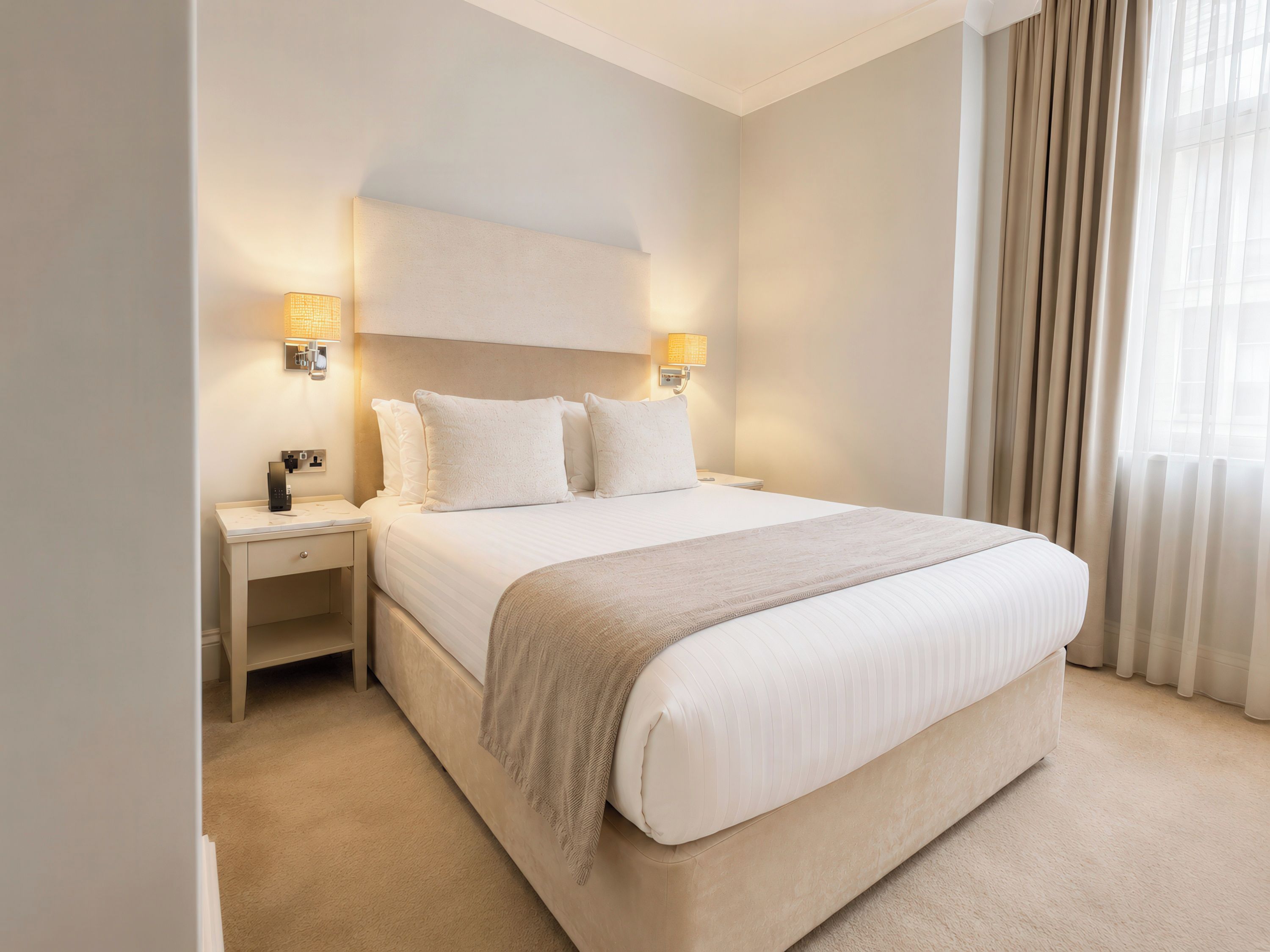 A hotel room with a large bed, bedside lamps, a nightstand, and a window with curtains.
