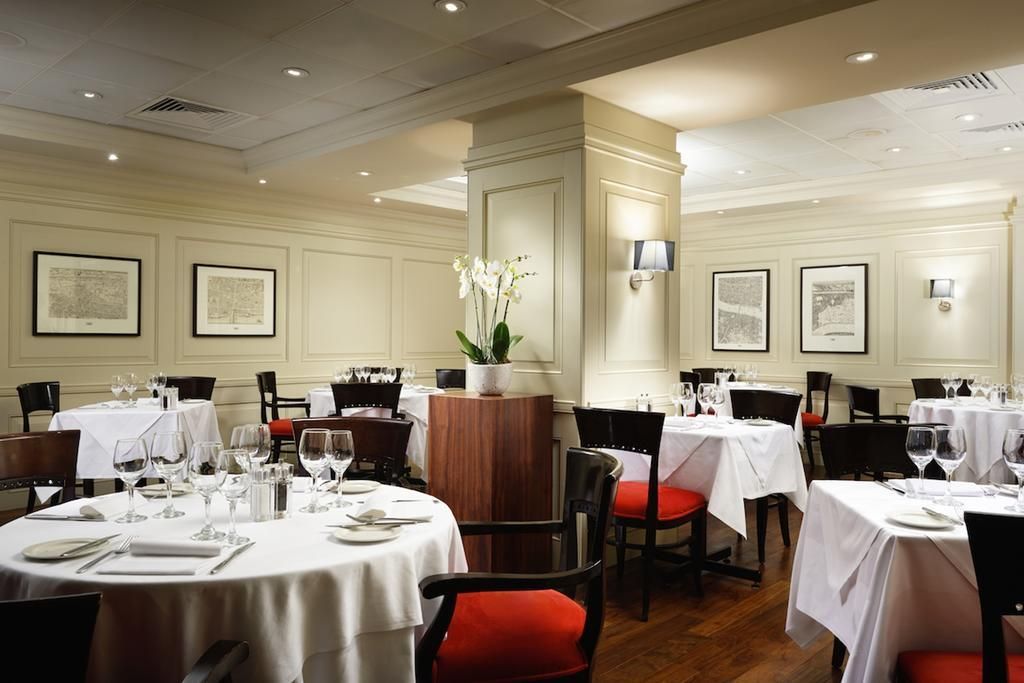 A dining area with round tables, chairs, and white tablecloths.