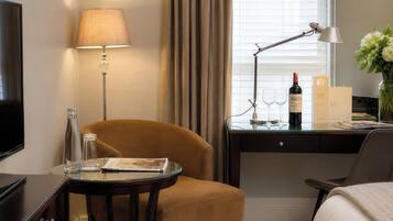 A hotel room with a bed, a desk with a lamp, a chair, a television, and a window with curtains.