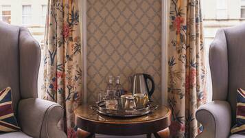 A room with two armchairs, a small table with a tray of tea and glasses, and floral curtains.