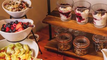 Mesa de buffet com diversas opções de comida, incluindo tigelas com frutas mistas, um copo de sobremesa em camadas e potes de granola.