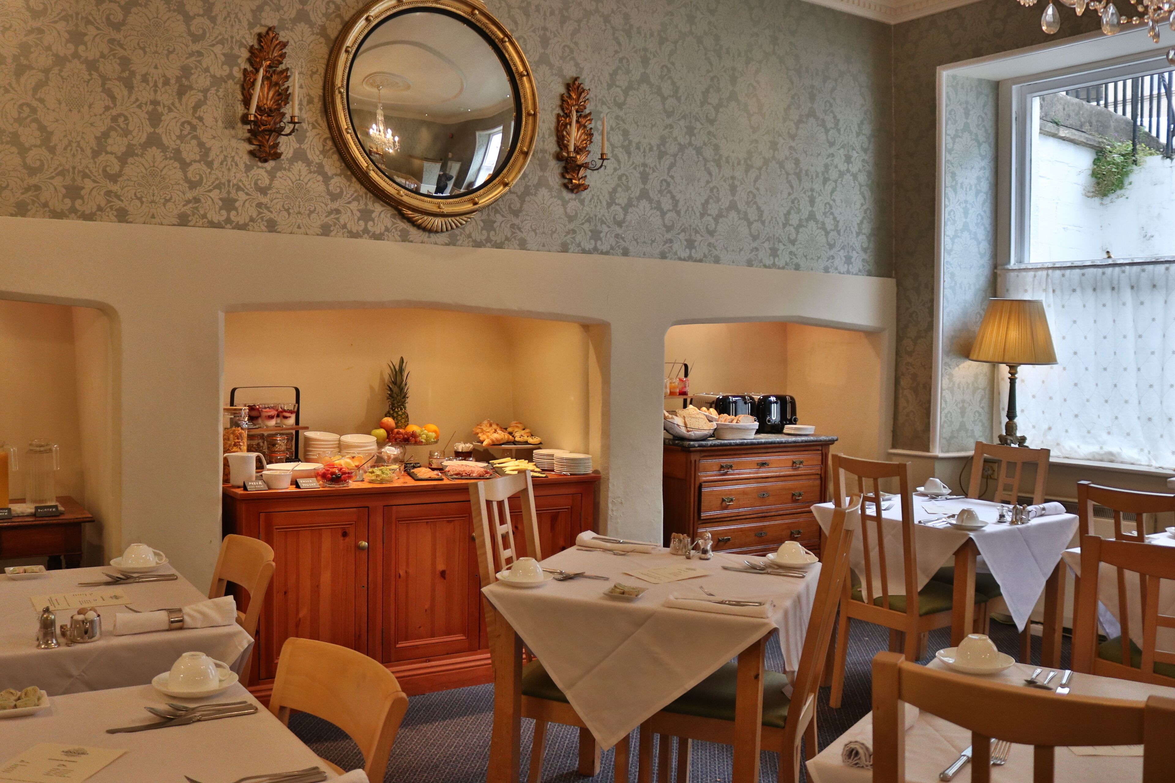 A dining area with tables set for meals, a mirror on the wall, and a window with curtains.