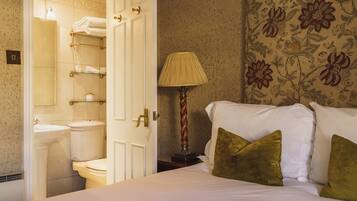 Ein Hotelzimmer mit Bett, Nachttisch, Lampe und einem Badezimmer inklusive Toilette und Handtuchhaltern.