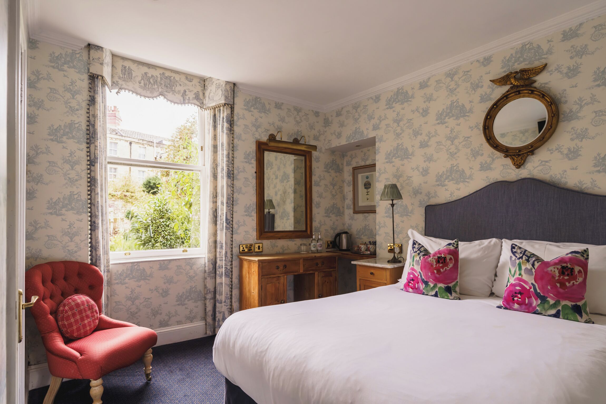 Quarto com uma cama grande, cómoda de madeira, poltrona vermelha e janela com cortinas.