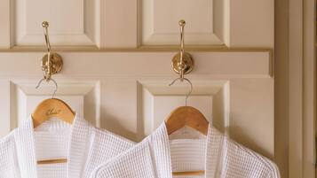 Dos batas blancas colgadas en una percha de madera frente a una puerta color crema con un panel decorativo.