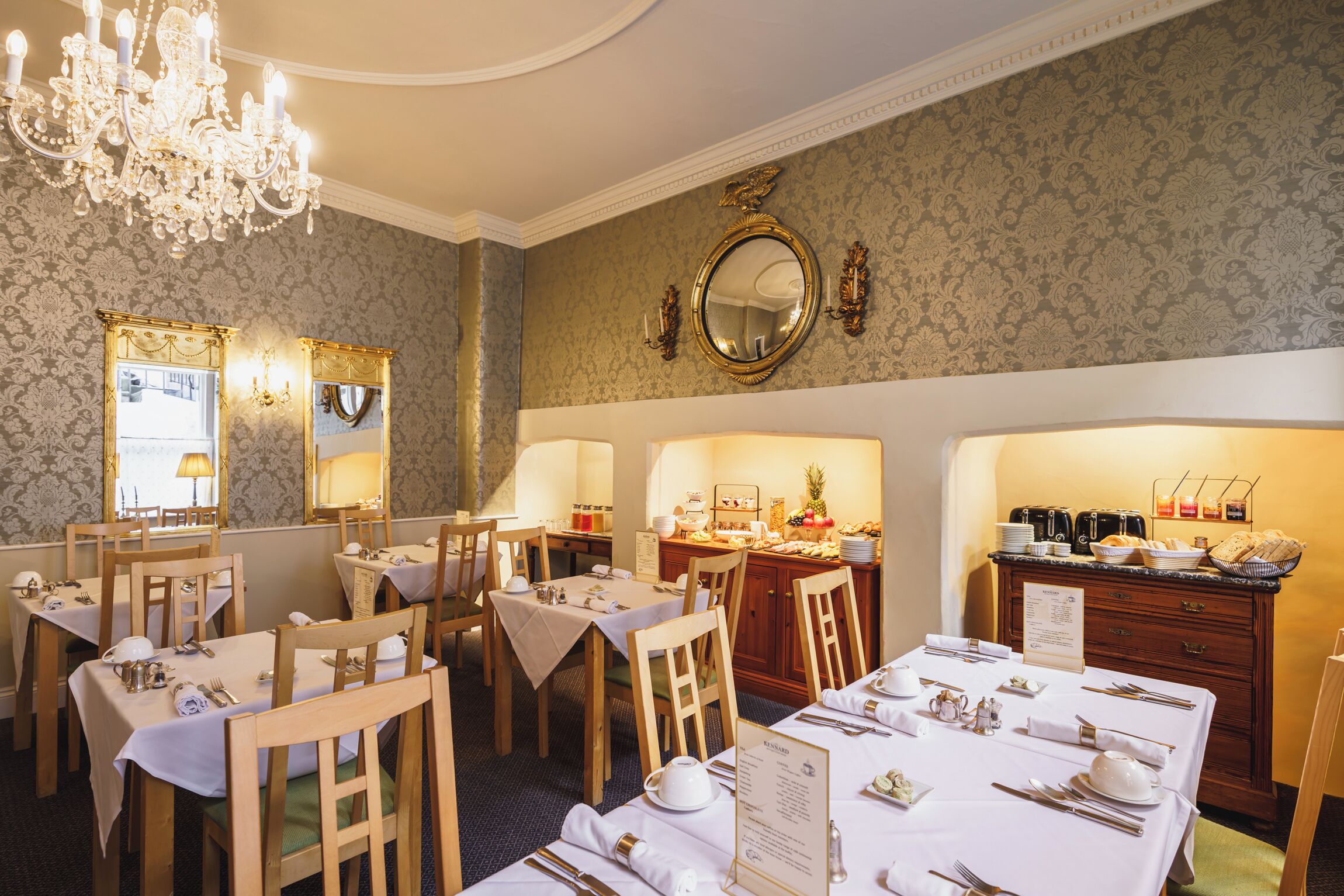 En elegant spisesal med flere dækketøjsbord, en lysekrone og et buffetbord.
