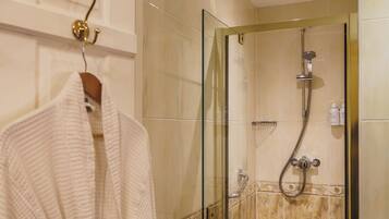 A bathroom with a glass-enclosed shower, a towel rack with a white towel, and a small shelf with toiletries.